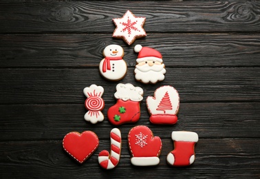 Photo of Christmas tree shape made of delicious decorated gingerbread cookies on black wooden table, flat lay