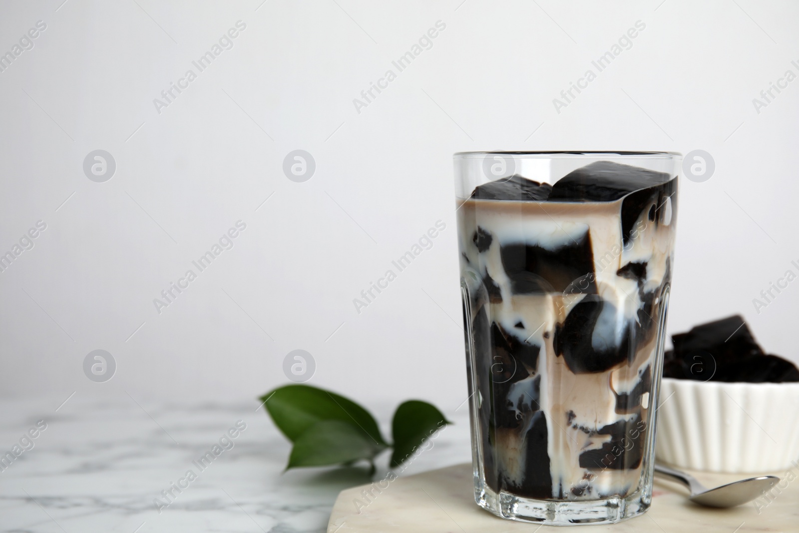 Photo of Glass of milk with grass jelly on white marble table. Space for text