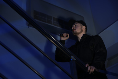 Photo of Male security guard with flashlight on stairs in darkness