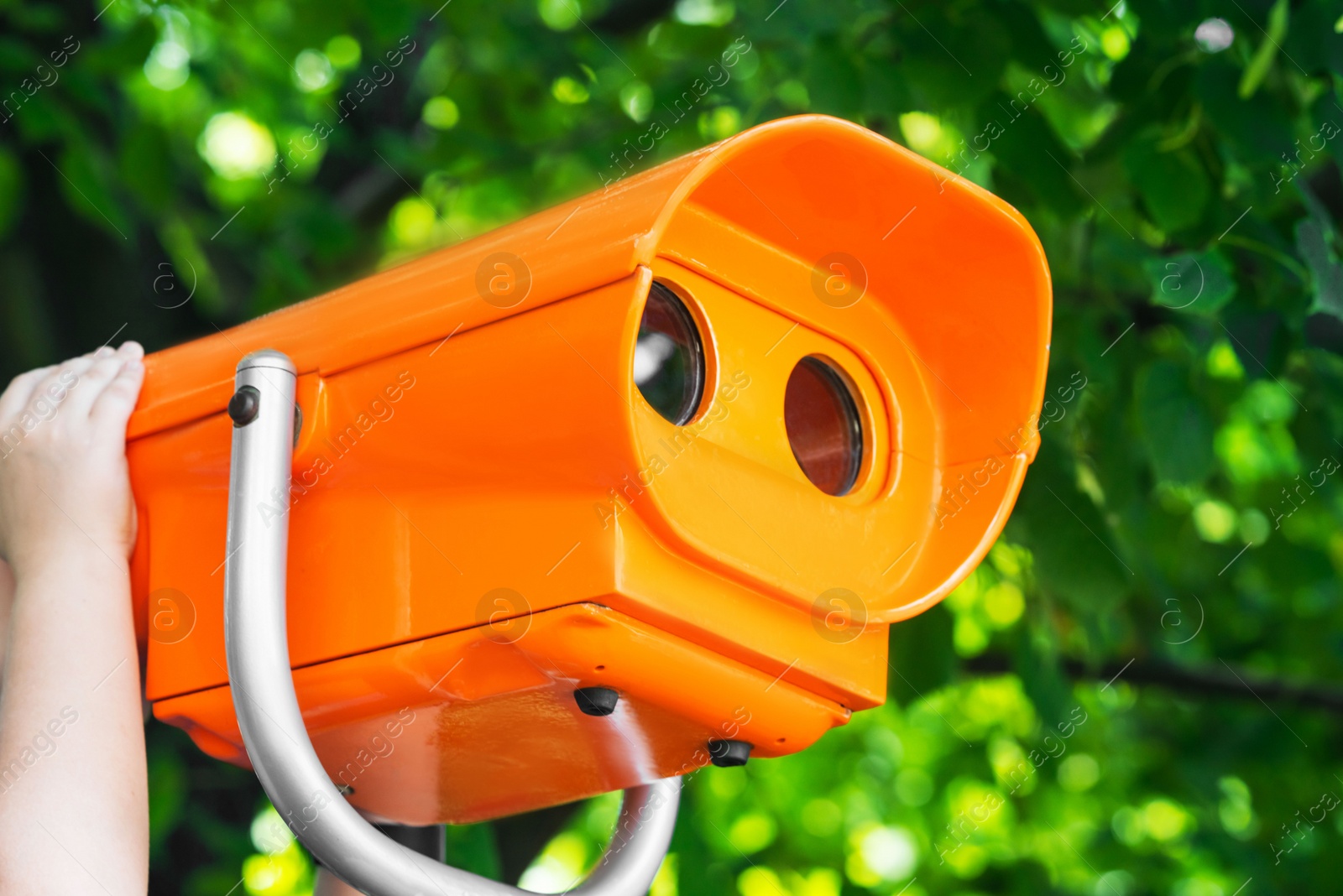 Photo of Girl looking through mounted binoculars outdoors on sunny day, closeup