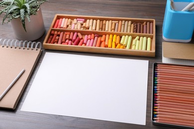 Photo of Blank sheet of paper, colorful chalk pastels and drawing pencils on wooden table. Modern artist's workplace