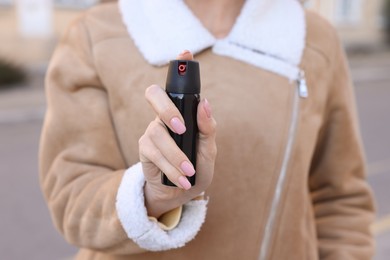 Photo of Young woman using pepper spray outdoors, closeup