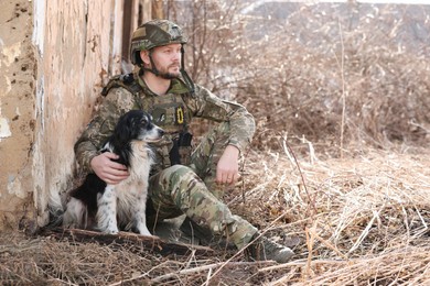 Photo of Ukrainian soldier with stray dog sitting outdoors. Space for text