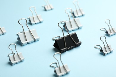 Photo of Black paper binder clip among white ones on light blue background. Racism concept