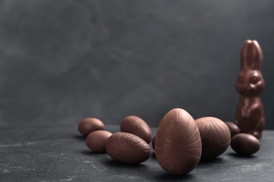 Photo of Sweet chocolate eggs and bunny on black table. Space for text
