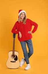 Photo of Young woman in Santa hat with acoustic guitar on yellow background. Christmas music