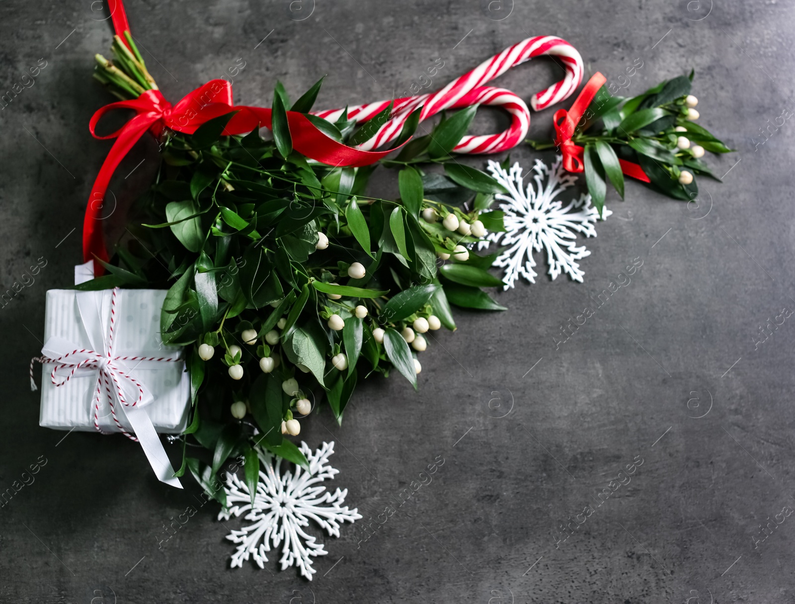 Photo of Mistletoe bunches, gift box, decorations and space for text on grey background, above view. Traditional Christmas decor