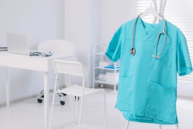 Photo of Turquoise medical uniform and stethoscope on rack in clinic. Space for text