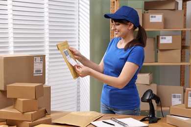 Photo of Parcel packing. Post office worker sticking barcode on bag at wooden table indoors