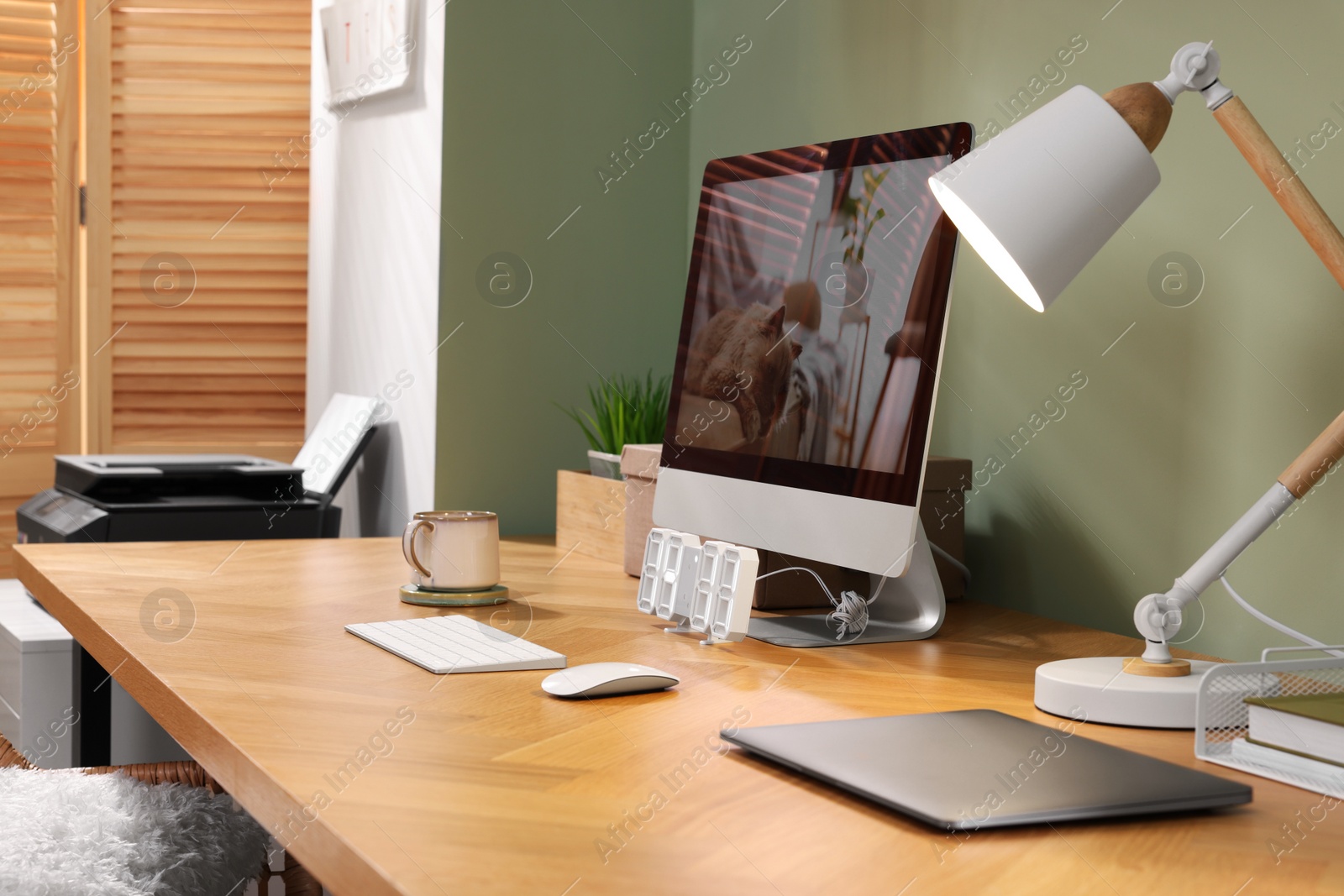 Photo of Stylish workplace with computer, laptop and lamp near olive wall at home