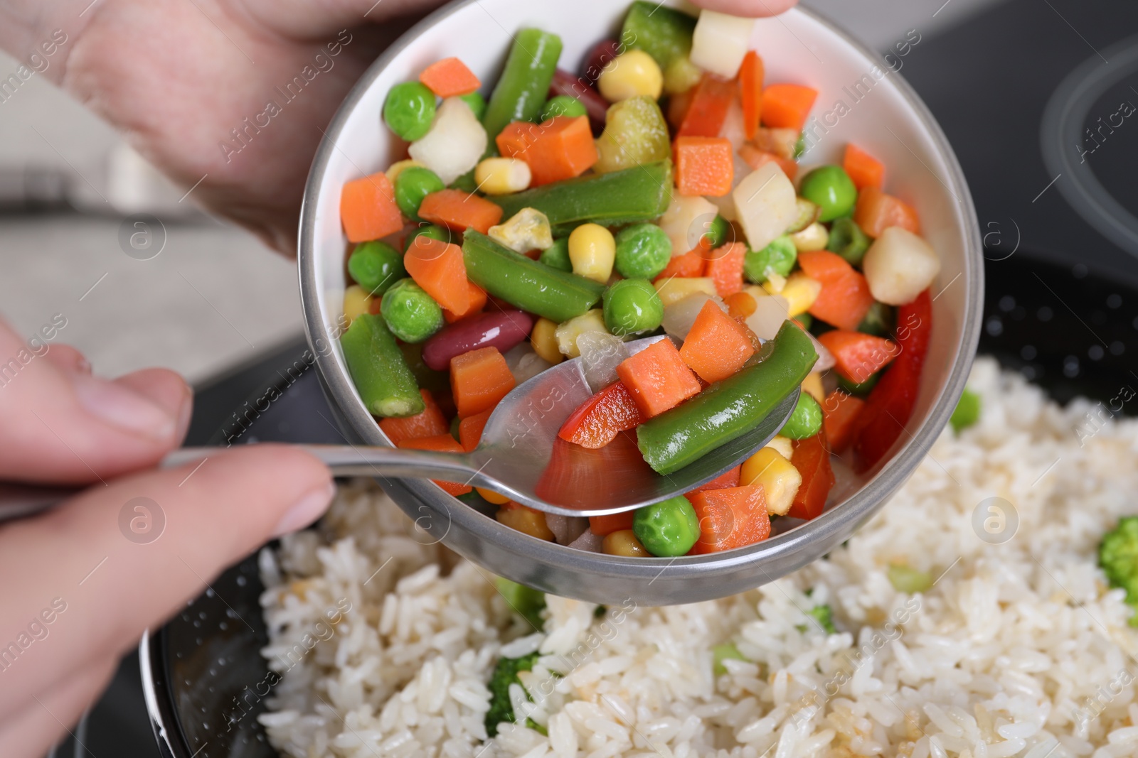 Photo of Woman cooking tasty rice with vegetables on induction stove, closeup