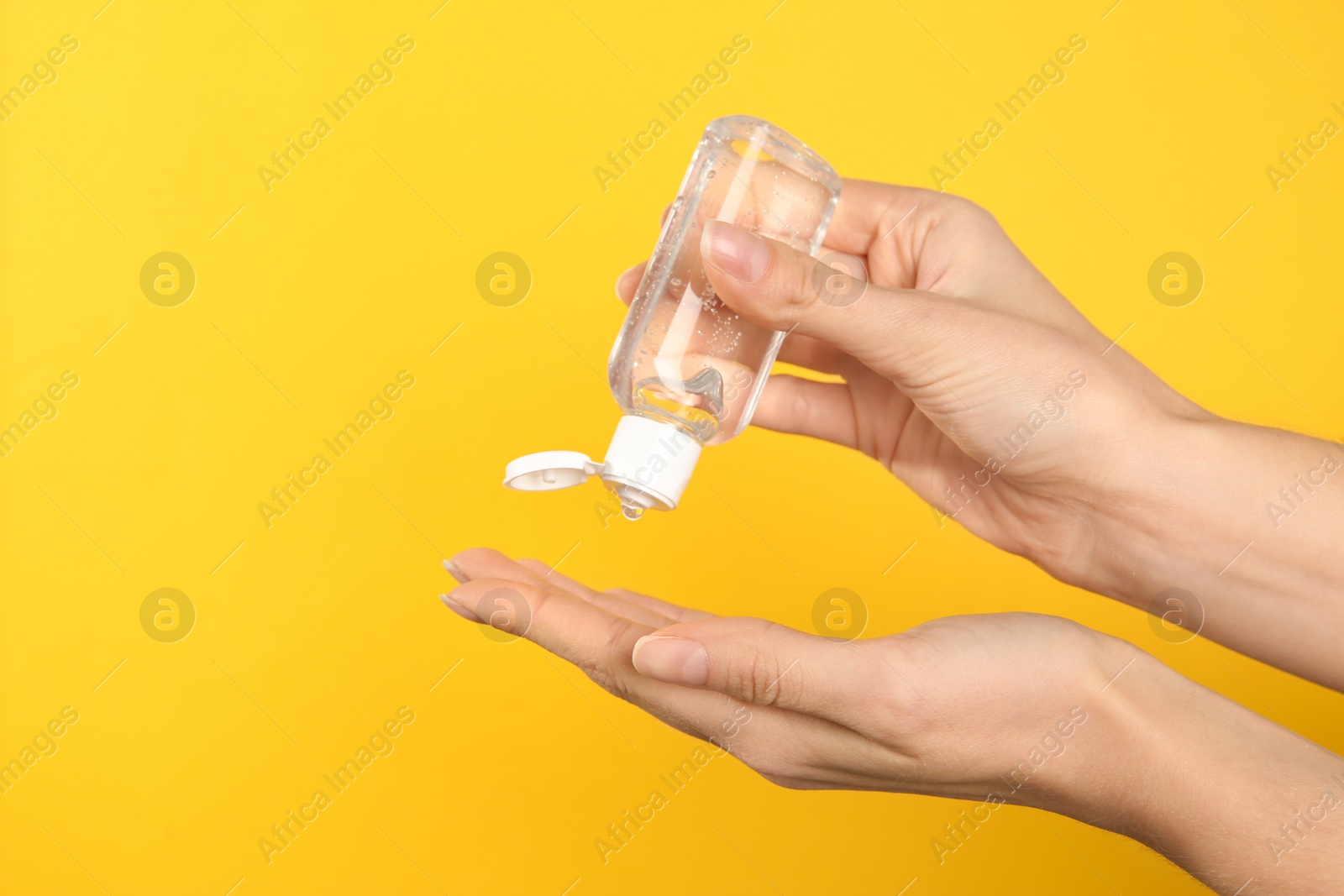 Photo of Woman applying antiseptic gel on yellow background, closeup