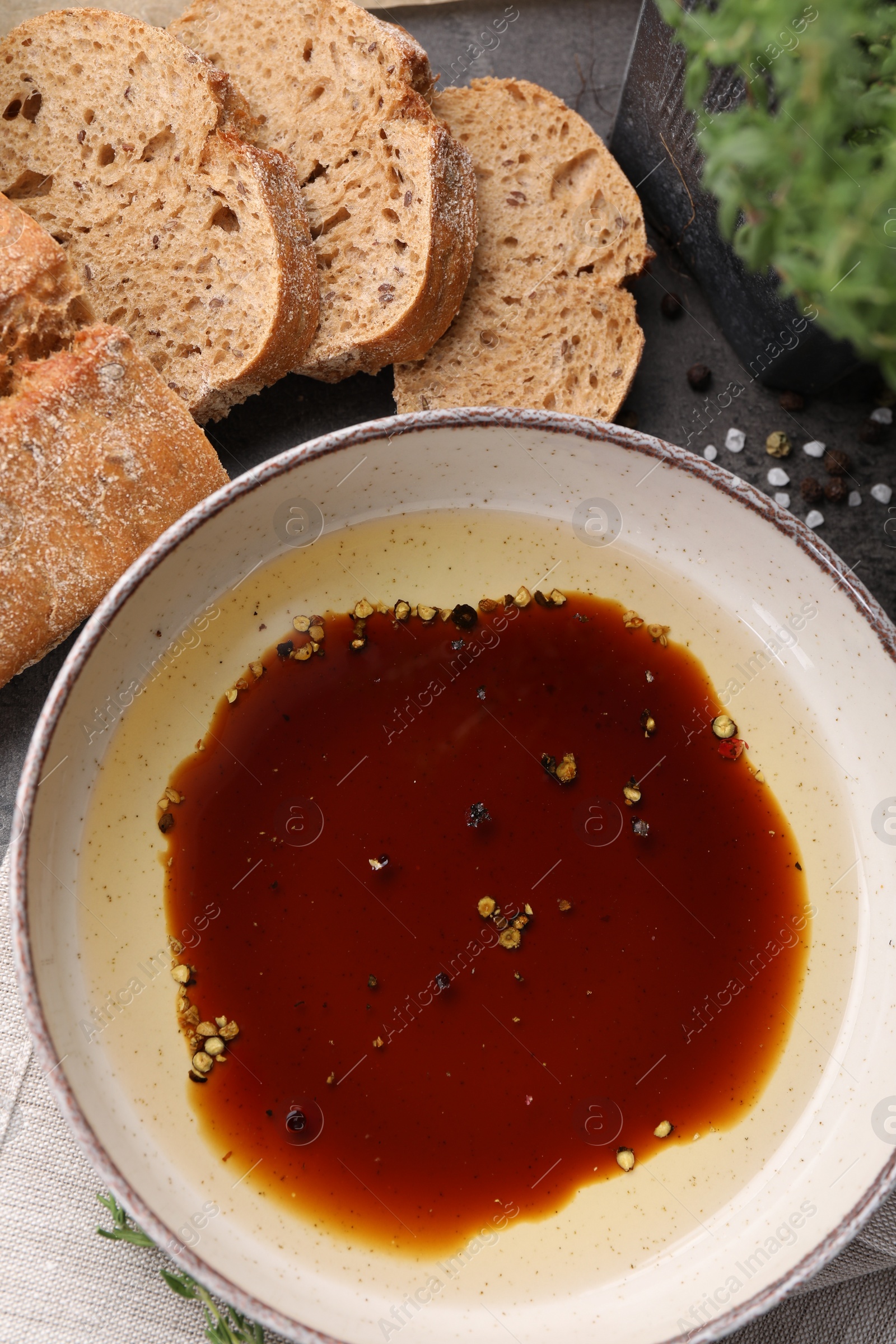 Photo of Bowl of balsamic vinegar with oil, spices and bread on dark grey table, flat lay
