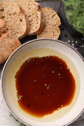 Bowl of balsamic vinegar with oil, spices and bread on dark grey table, flat lay
