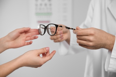 Photo of Male ophthalmologist helping woman choose glasses in clinic, closeup
