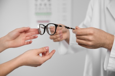 Male ophthalmologist helping woman choose glasses in clinic, closeup