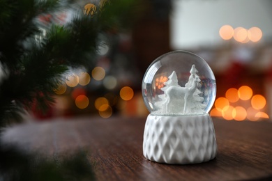 Snow globe on wooden table against blurred background, space for text. Bokeh effect