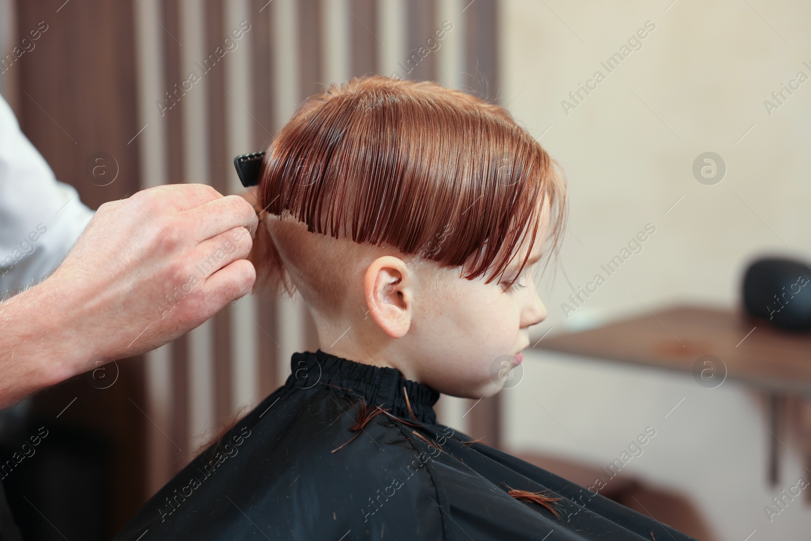 Photo of Professional hairdresser cutting boy's hair in beauty salon, closeup