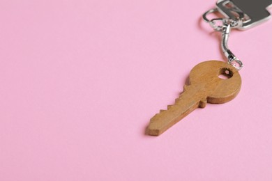 Photo of Wooden keychain in shape of key on pale pink background, closeup. Space for text