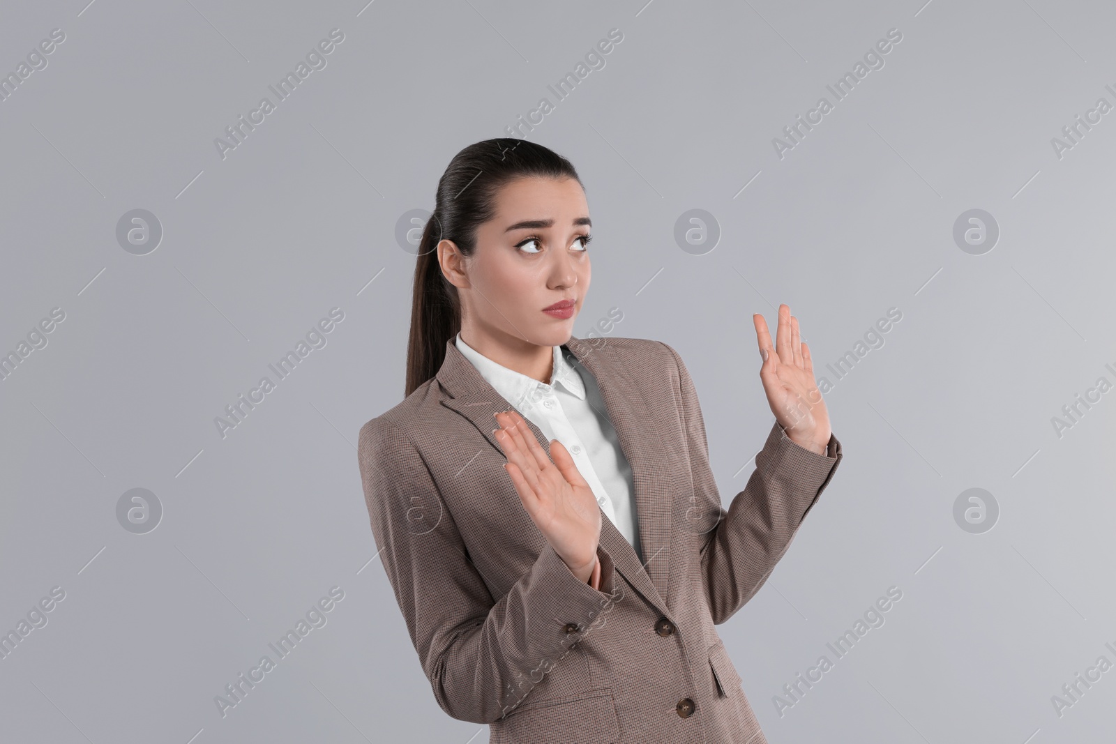 Photo of Young woman in suit avoiding something on light grey background