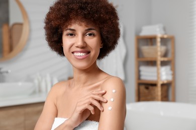 Photo of Beautiful young woman applying body cream onto arm in bathroom, space for text