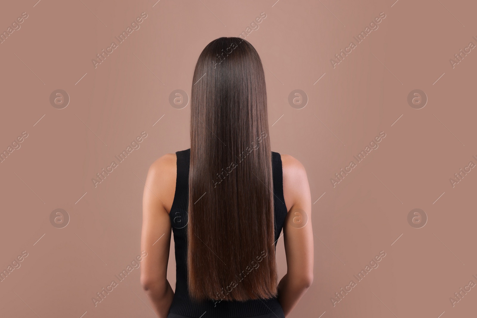 Photo of Hair styling. Woman with straight long hair on pale brown background, back view