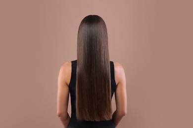 Photo of Hair styling. Woman with straight long hair on pale brown background, back view