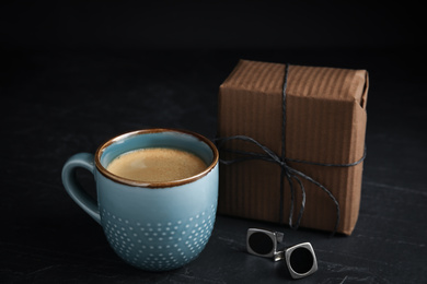 Photo of Cup of coffee, gift box and cuff links on black table. Happy father's day