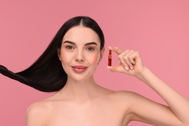 Beautiful young woman with long healthy hair holding ampoule on pink background