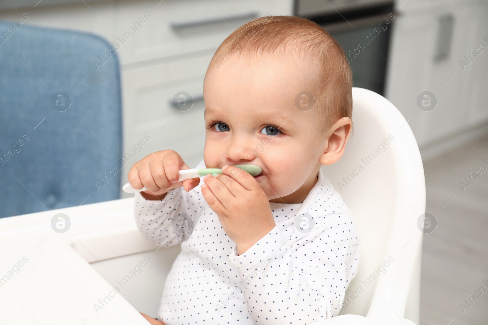 Photo of Cute little baby with spoon in highchair at home