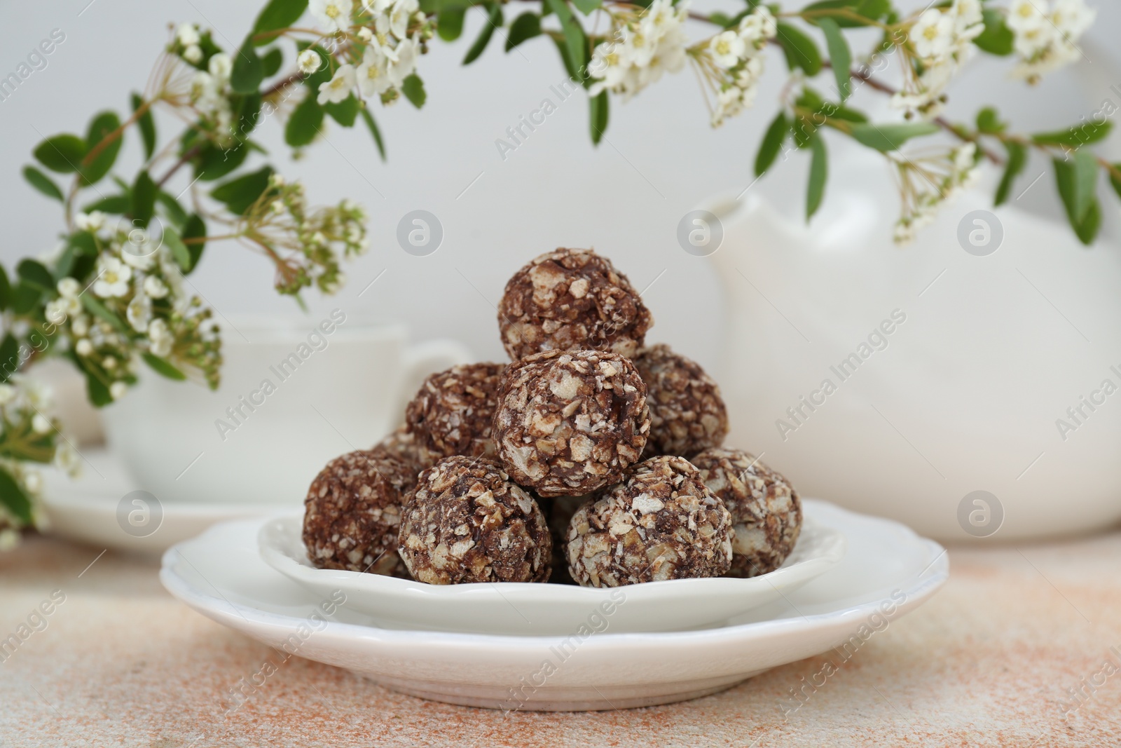 Photo of Delicious chocolate candies under blooming branch on beige table