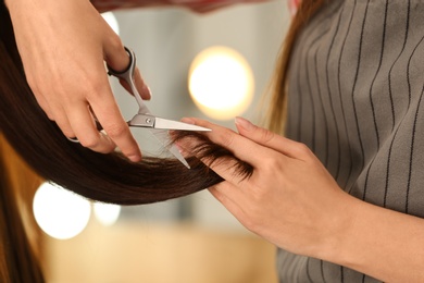 Photo of Barber making stylish haircut with professional scissors in beauty salon, closeup