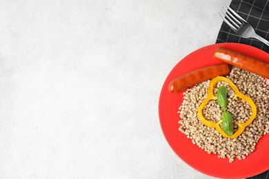 Photo of Tasty buckwheat porridge with sausages on light table, top view. Space for text