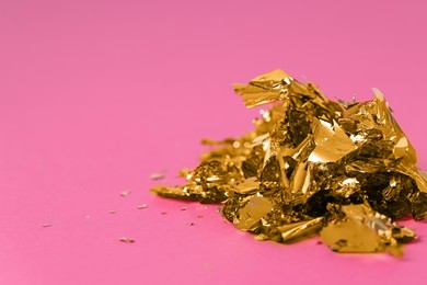 Photo of Pieces of edible gold leaf on pink background, closeup. Space for text