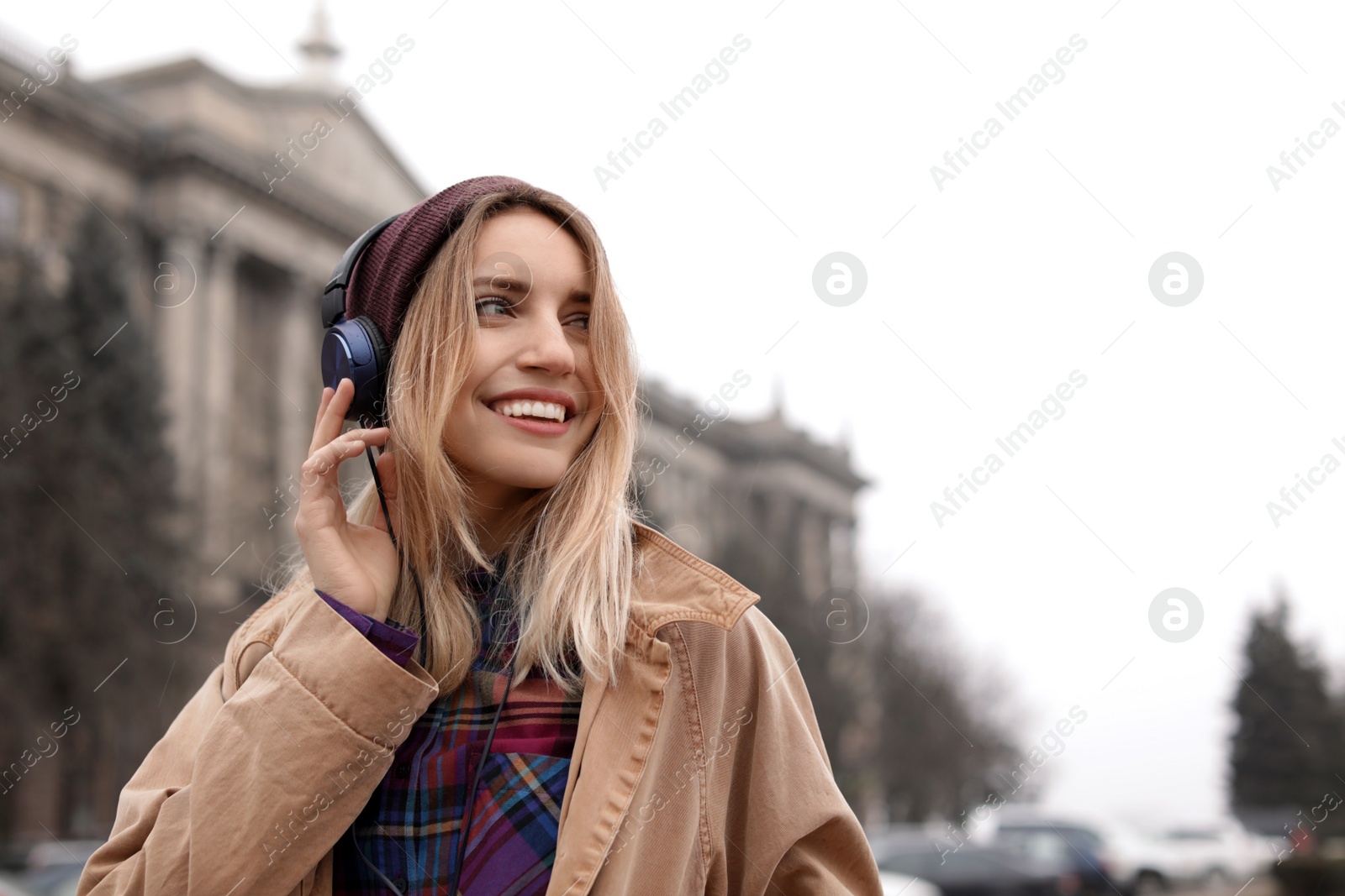 Photo of Young woman with headphones listening to music outdoors. Space for text