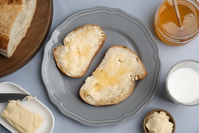Photo of Sandwiches with butter, honey and milk on light grey table, flat lay