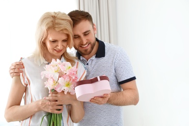 Photo of Young man congratulating his mature mom at home, space for text. Happy Mother's Day