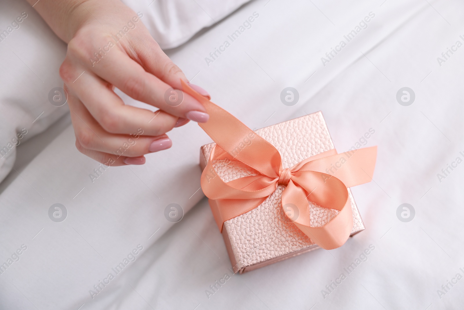 Photo of Woman opening gift box on bed, closeup