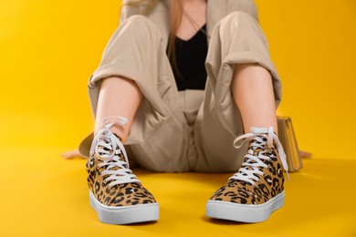 Woman wearing classic old school sneakers with leopard print on orange background, closeup