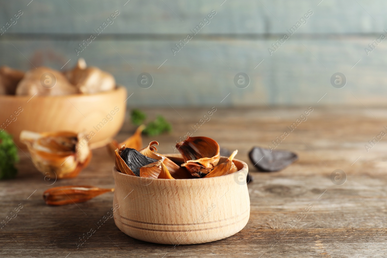 Photo of Bowl of black garlic on wooden table. Space for text
