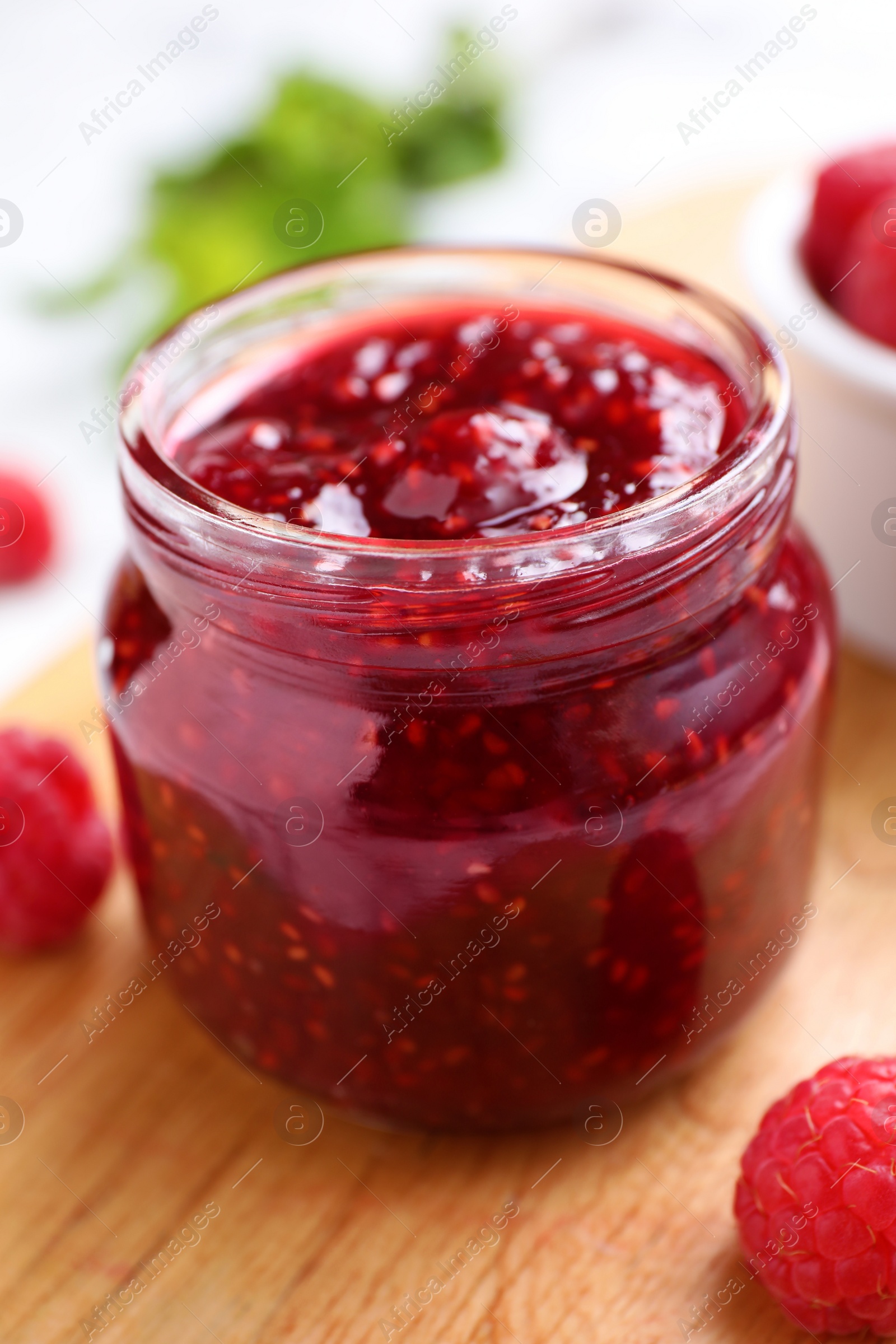 Photo of Delicious jam and fresh raspberries on wooden board, closeup