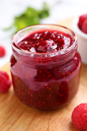 Delicious jam and fresh raspberries on wooden board, closeup