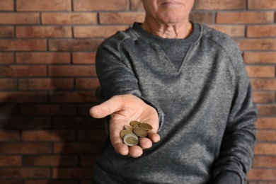 Photo of Poor elderly man begging for money near brick wall, focus on hand