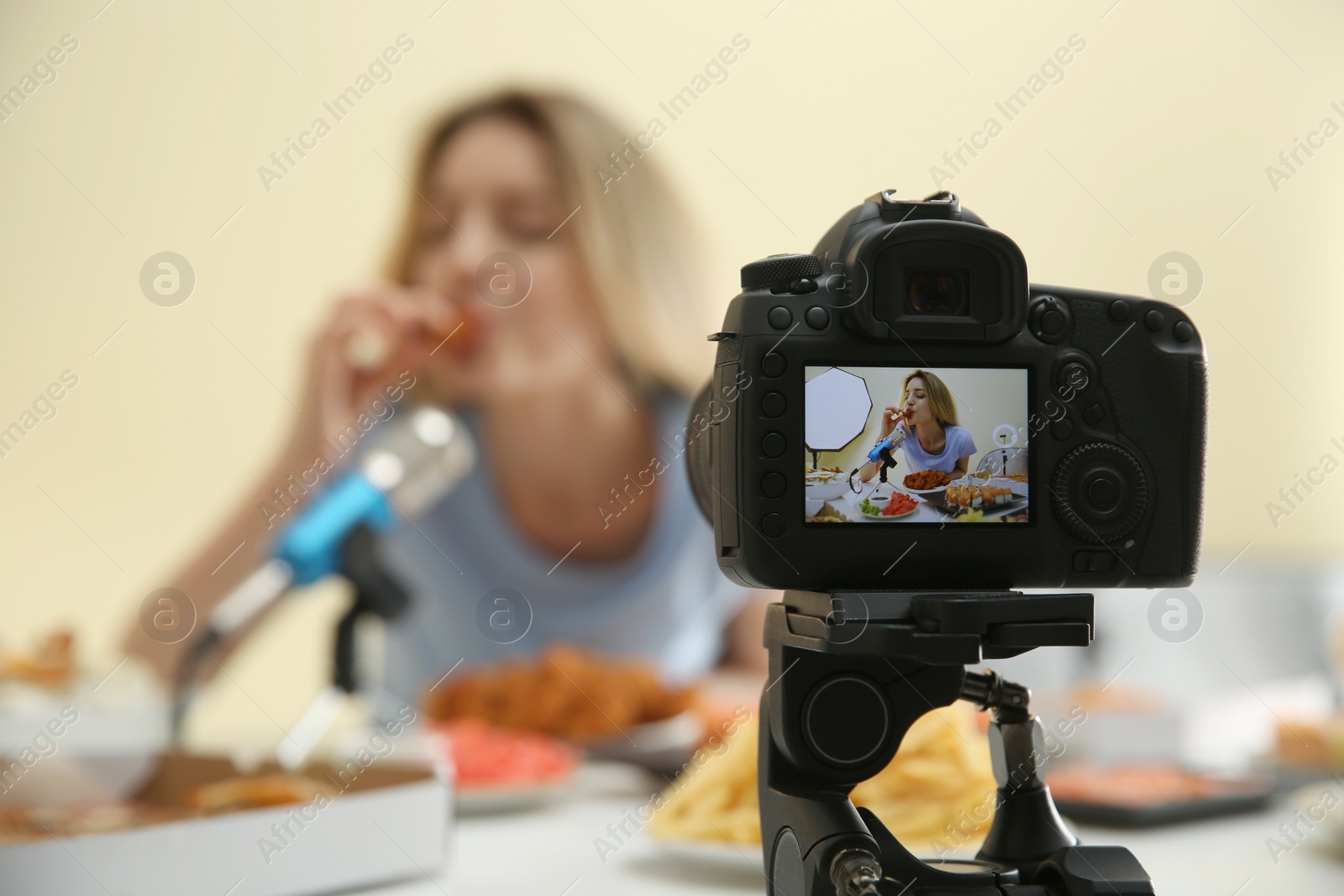 Photo of Food blogger recording eating show against light background, focus on camera screen. Mukbang vlog