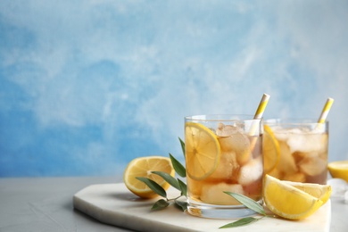 Glasses of lemonade with ice cubes and fruit on table against color background. Space for text