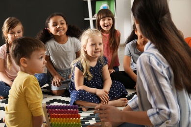 Photo of Cute little children with nursery teacher in kindergarten. Indoor activity