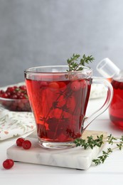 Photo of Tasty hot cranberry tea with thyme and fresh berries in glass cup on white wooden table