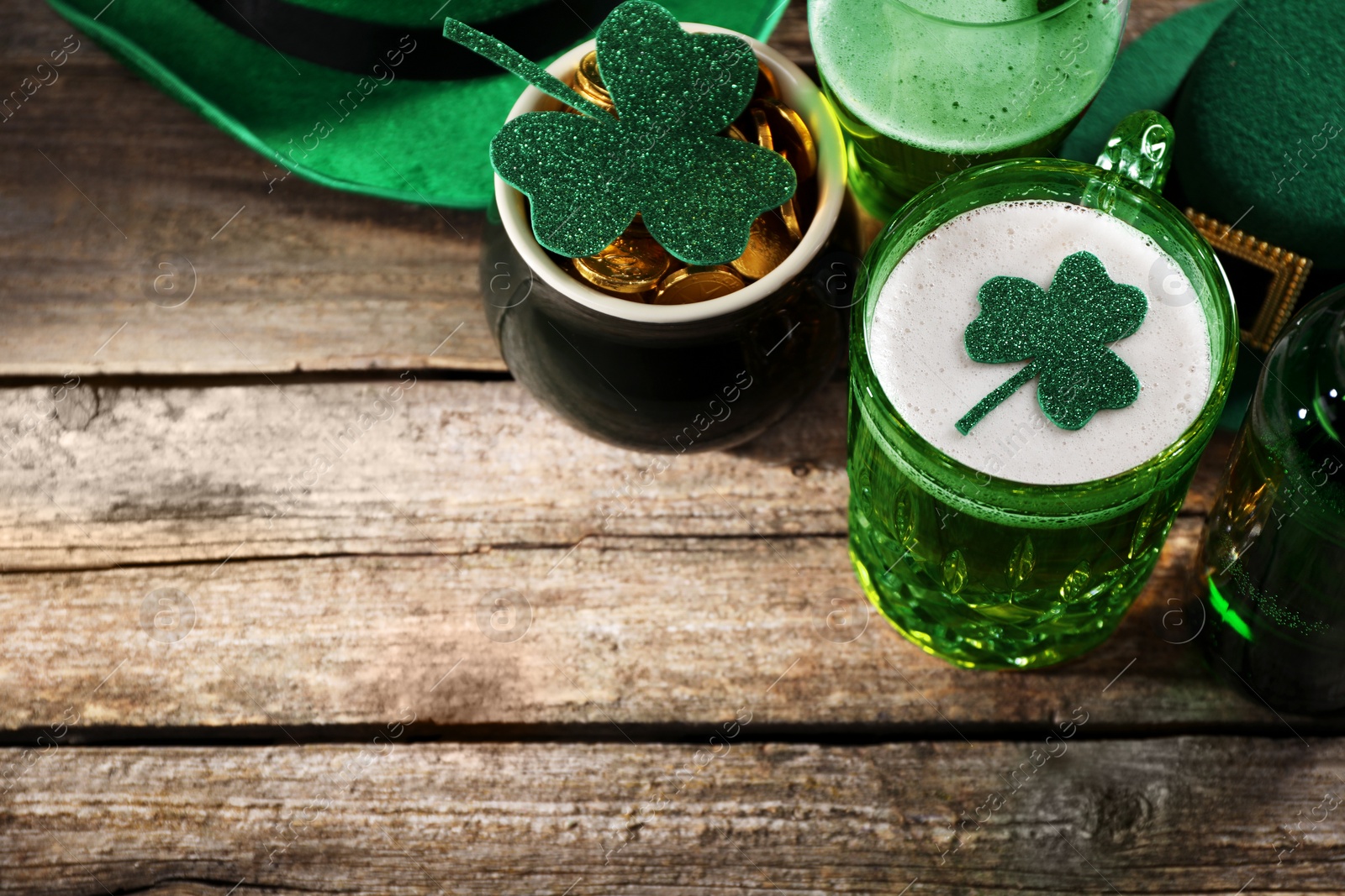 Photo of St. Patrick's day party. Green beer, leprechaun pot of gold and decorative clover leaves on wooden table, above view. Space for text