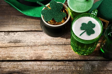 Photo of St. Patrick's day party. Green beer, leprechaun pot of gold and decorative clover leaves on wooden table, above view. Space for text