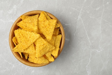 Wooden bowl with tasty Mexican nachos chips on grey table, top view. Space for text